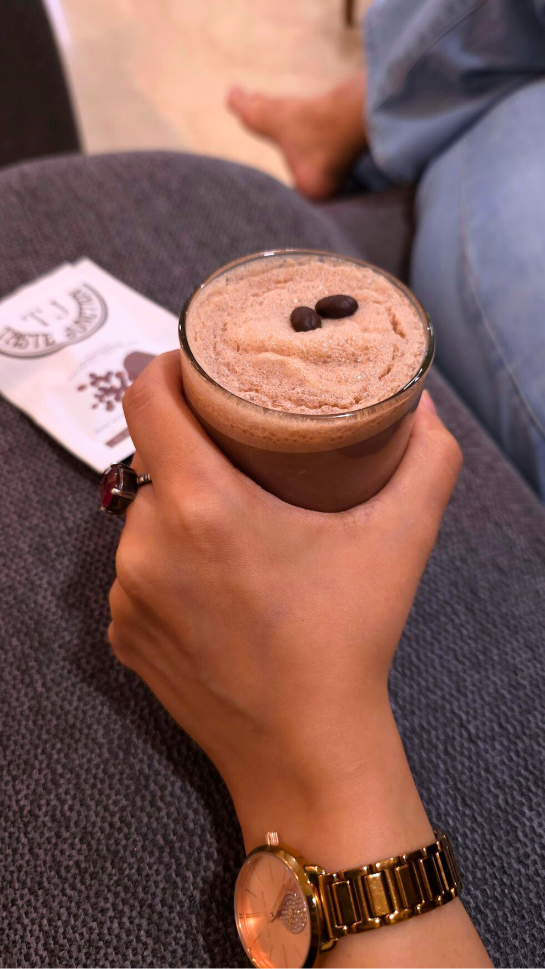 Hand holding a coffee cup with a lid and two beans on a textured surface.