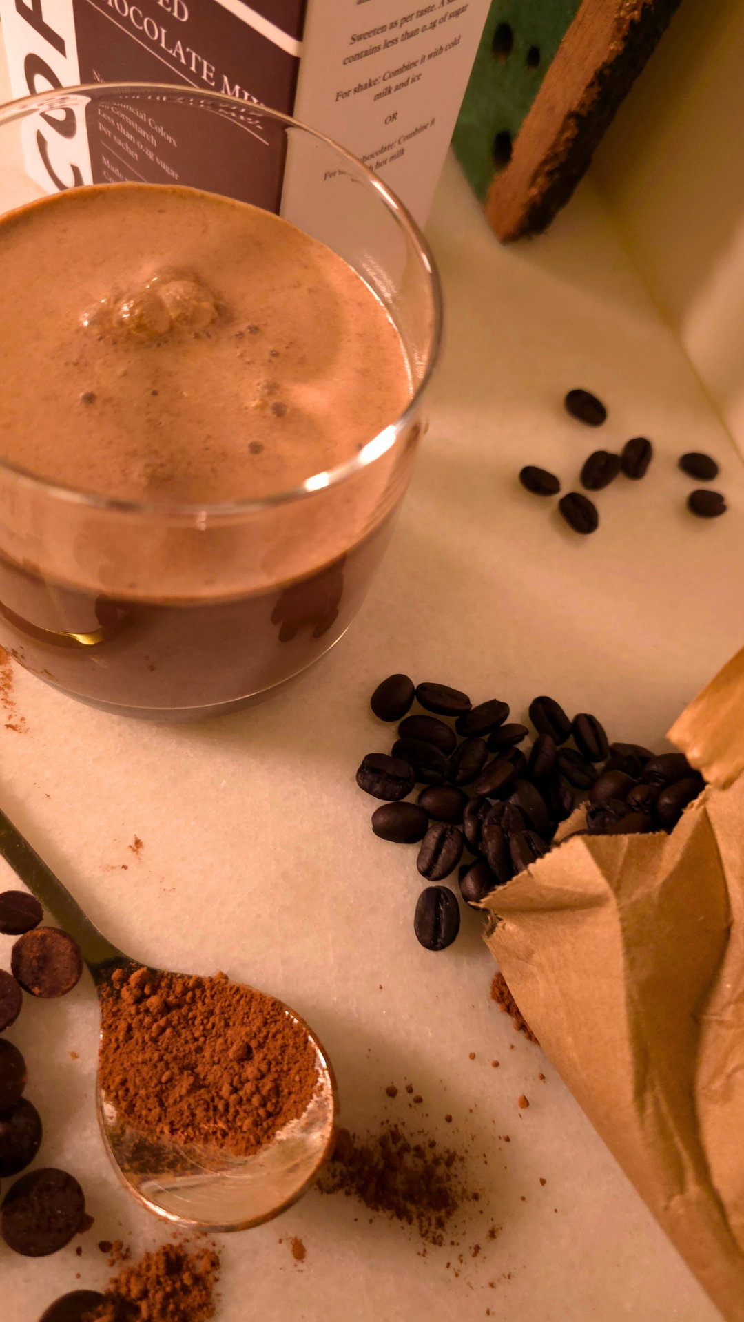 Glass of coffee with coffee beans and a scoop of ground coffee on a light surface.